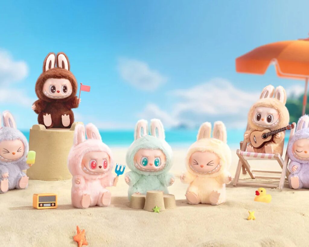 Plusieurs peluches Labubu vêtues de costumes de lapin jouent et se détendent sur une plage ensoleillée avec des châteaux de sable, des guitares et des parasols.