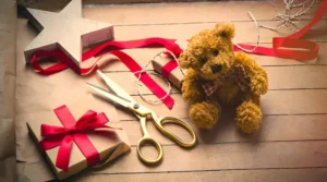 Teddy bear, scissors, ribbons, and wrapped gift on wooden table.