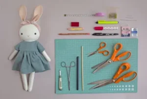 Sewing tools arranged neatly next to a stuffed bunny doll in a blue dress.