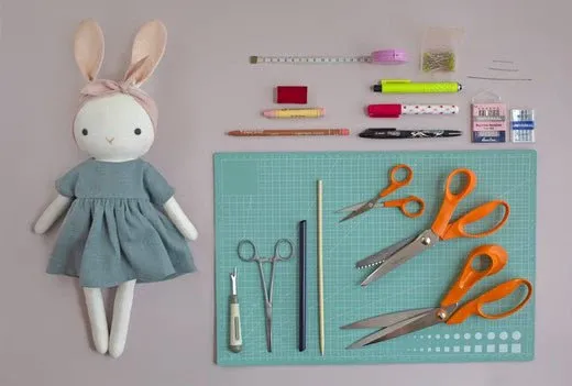 Sewing tools arranged neatly next to a stuffed bunny doll in a blue dress.