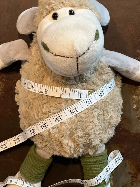 Soft plush sheep toy wrapped with white measuring tape on brown surface