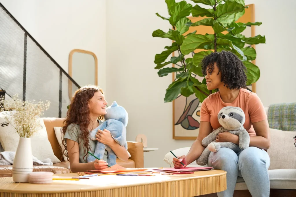 Girls holding stuffed animals while drawing at table in living room