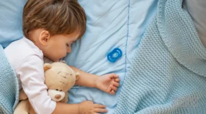 Child cuddling teddy bear while sleeping under blue blanket