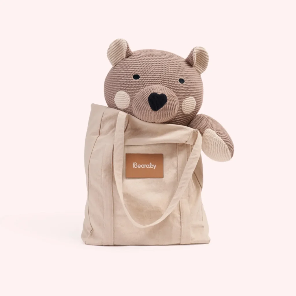Brown knitted bear toy inside a beige tote bag labeled Bearaby