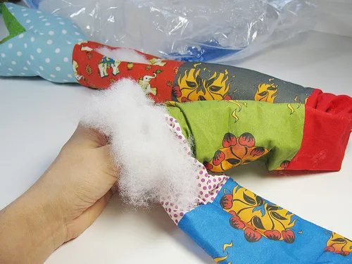 Hand holding stuffing material next to partially filled colorful fabric toy.