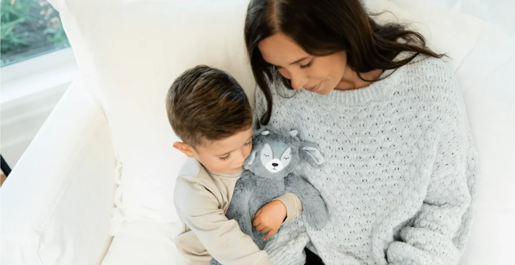 Mother and son cuddling gray plush toy on white couch