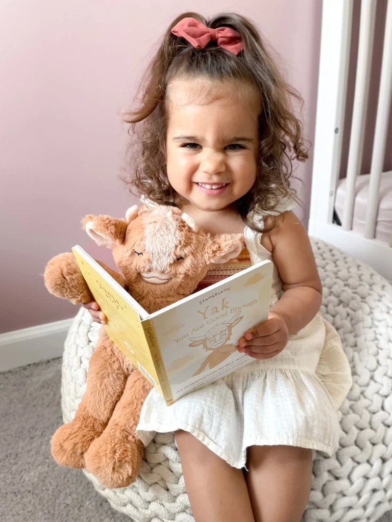 Little girl holding stuffed animal reading a book