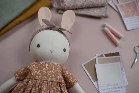Stuffed bunny doll wearing brown floral dress and headband on craft table.