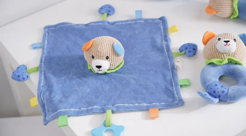 Soft baby plush toy on blue cloth with colorful tags.
