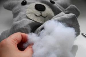 Hand inserting white stuffing into gray plush toy with stitched face.