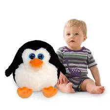 Baby sitting next to a large soft penguin toy with orange beak and feet.