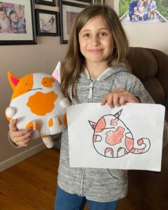 Girl holding a stuffed toy and drawing of an orange and white cat.