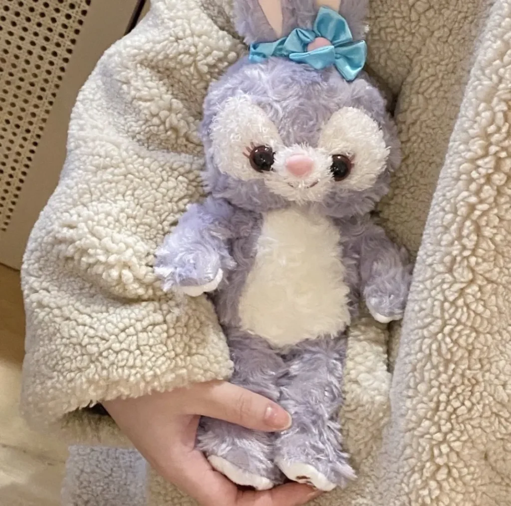 Hand holding a soft purple and white bunny plush toy with a blue bow.
