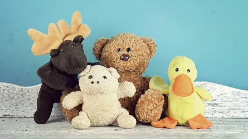 Plush moose, bear, pig, and duck sitting together on wooden surface with blue background.