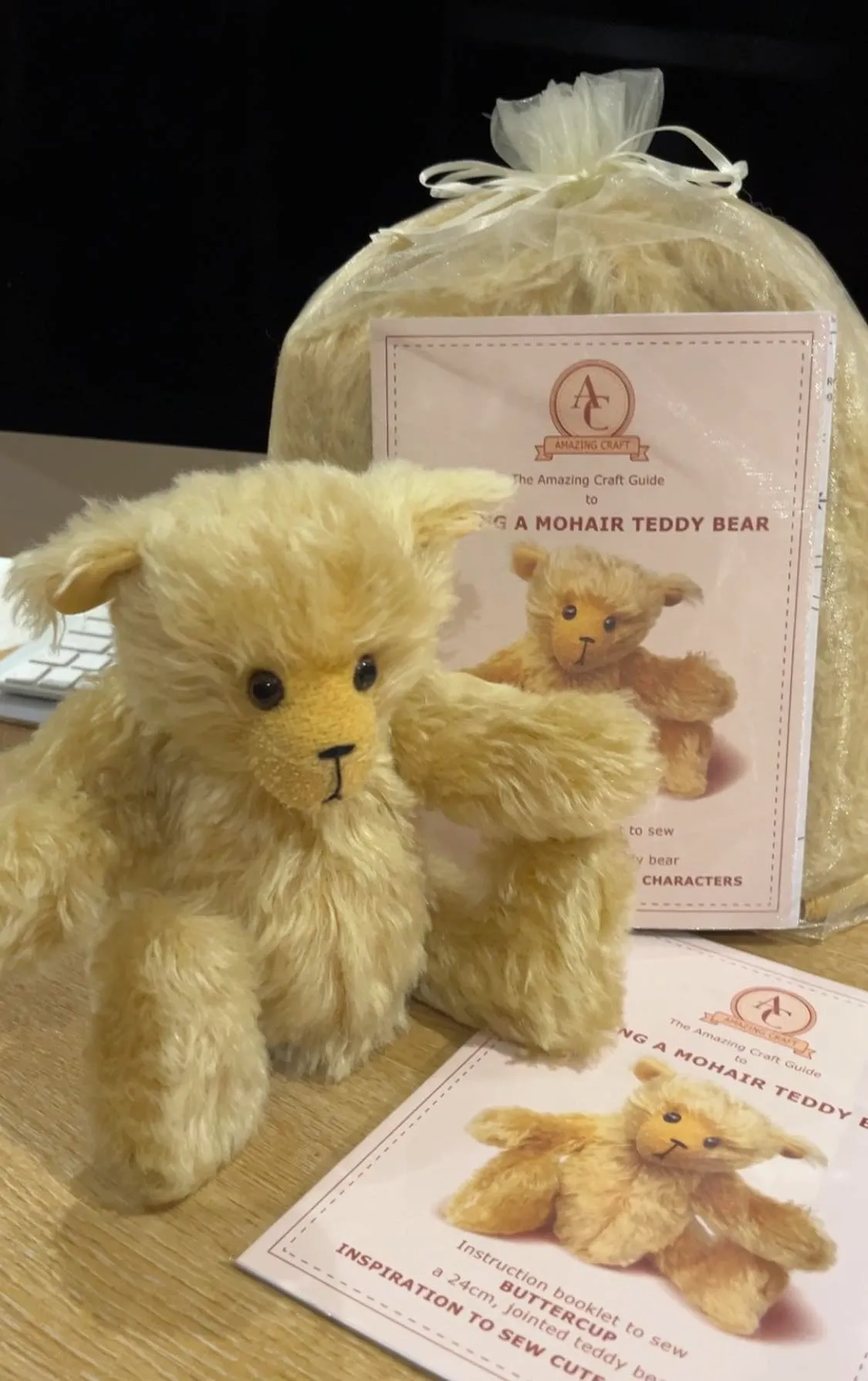 Soft mohair teddy bear with sewing guide and materials on table.
