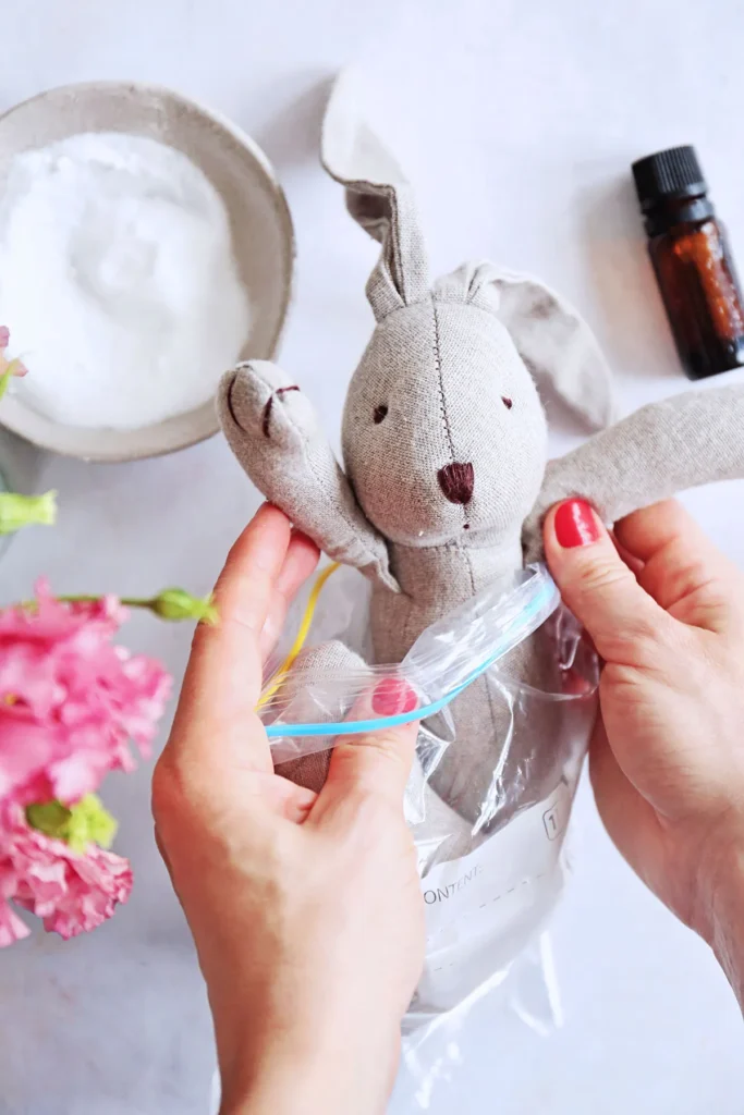 Hands placing stuffed bunny into a ziplock bag with cleaning supplies nearby.
