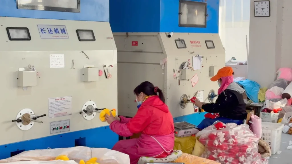 Workers stuffing plush toys using specialized machines in a factory setting.