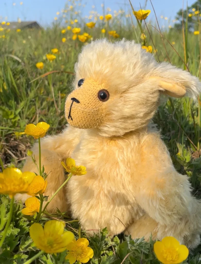 Mohair teddy bear sitting among bright yellow flowers outdoors.