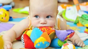 Baby lying on colorful play mat chewing a bright, multi-patterned soft toy.