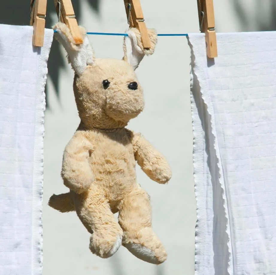Yellow stuffed bear hanging on clothesline with clothespins to dry.