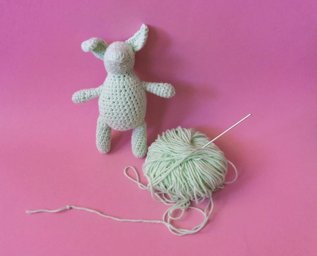 Handmade crochet toy with yarn and needle on pink background.
