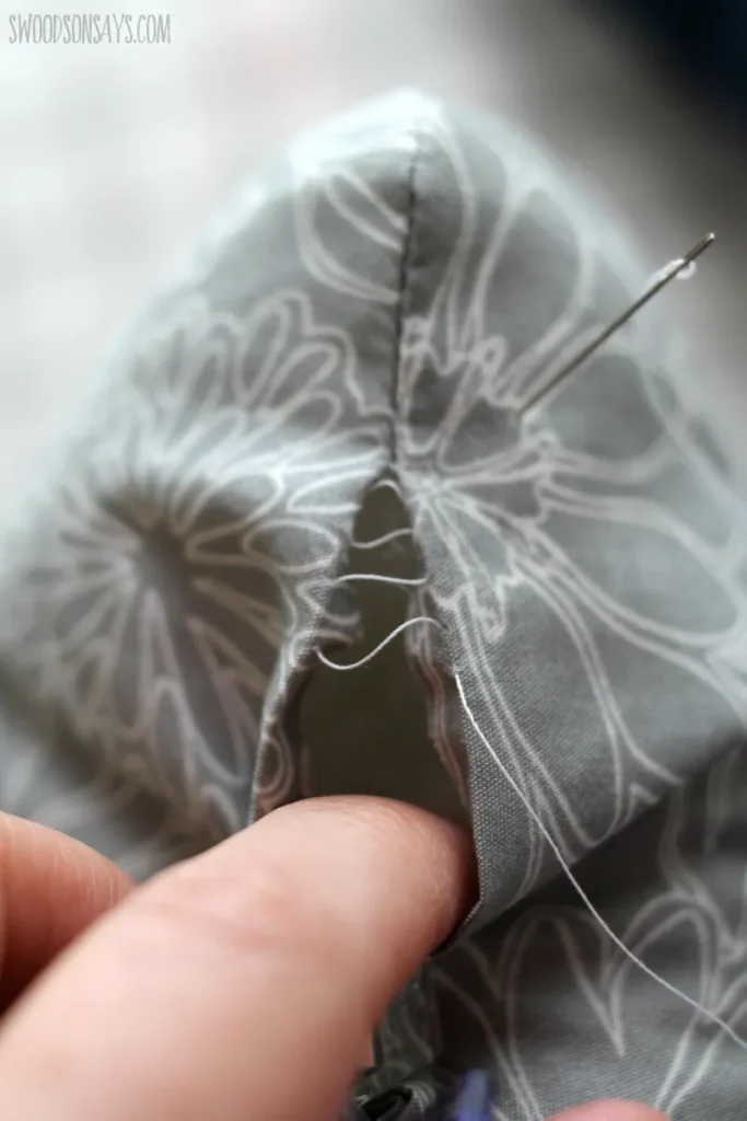 Hand sewing a ladder stitch on gray fabric.