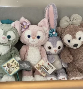 Four Disney plush toys sitting side by side on a couch with tags attached.