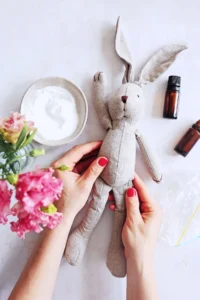 Hands holding stuffed bunny with baking soda and essential oils nearby.