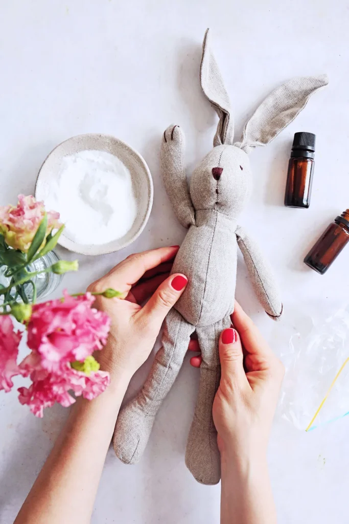 Hands holding stuffed bunny with baking soda and essential oils nearby.