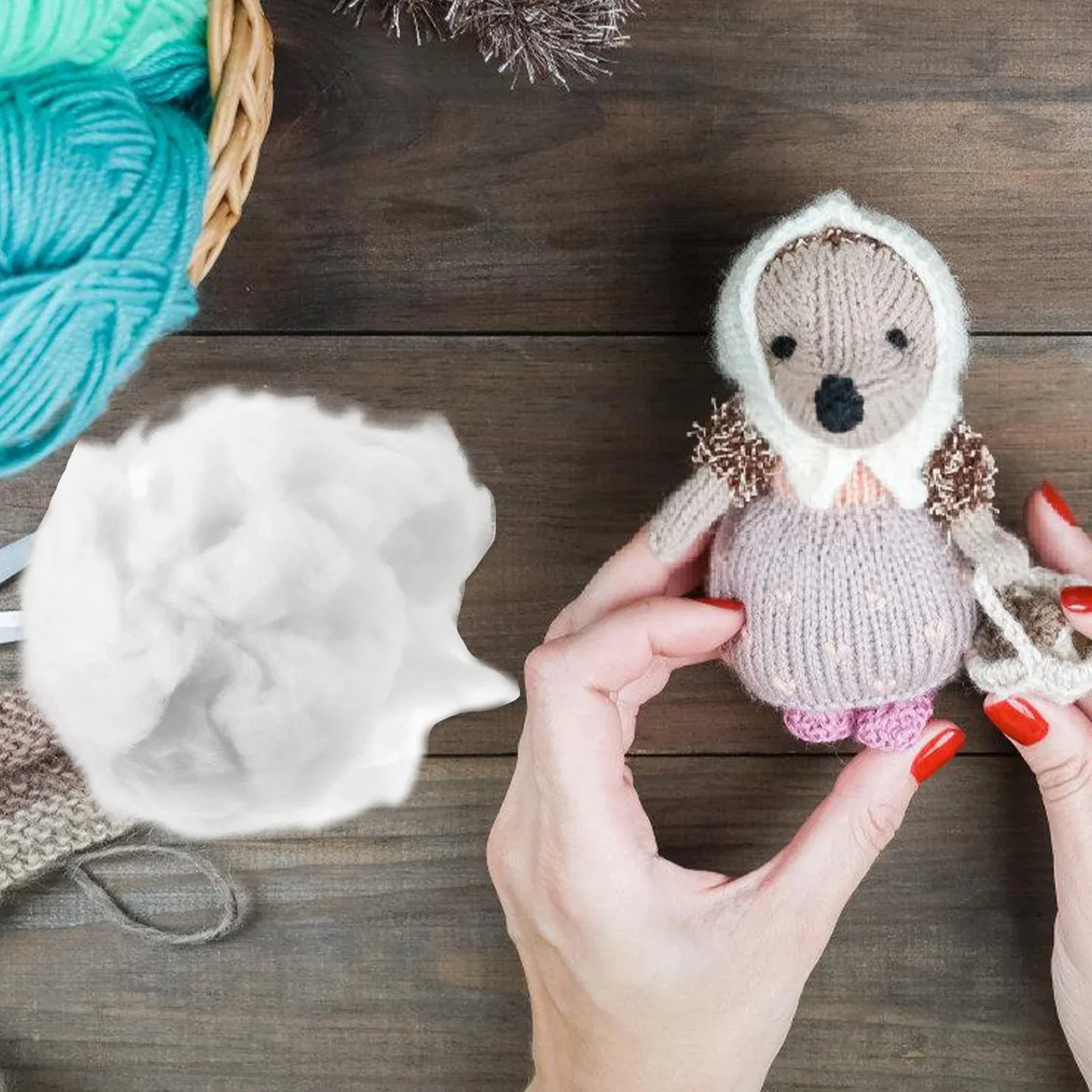 White stuffing material next to a knitted toy held by hands with red nails on a wooden surface