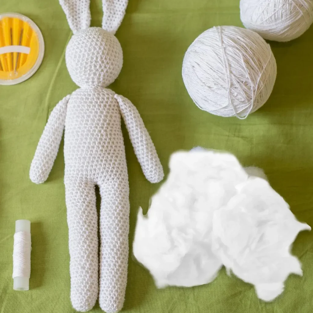 White crocheted bunny doll with yarn and fiber stuffing on green fabric background.