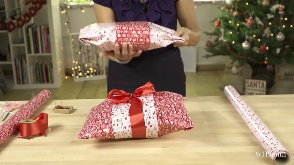 Person wrapping Christmas presents with red and white wrapping paper and red ribbon.