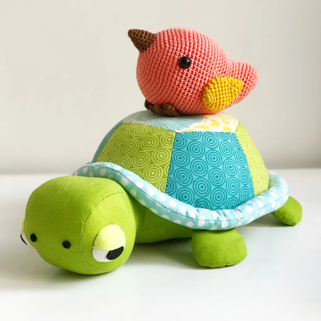 Soft toy turtle with patchwork shell and crocheted bird on top.