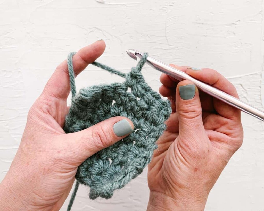 Hands crocheting with green yarn and a metal hook.