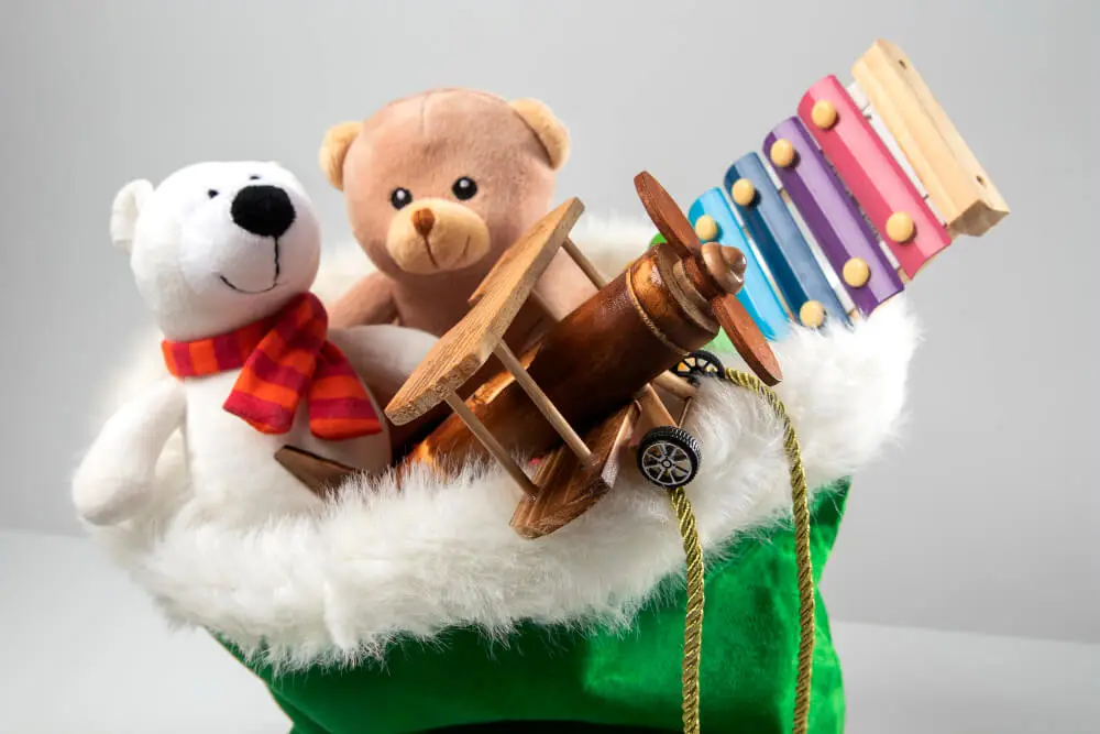Green Santa bag filled with plush polar bear, teddy bear, wooden airplane, and colorful xylophone.