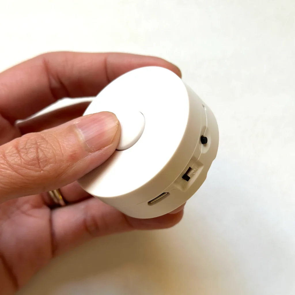 Hand pressing button on small white music module with USB port and switch.