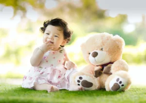 Smiling baby sitting on grass with a large teddy bear toy.