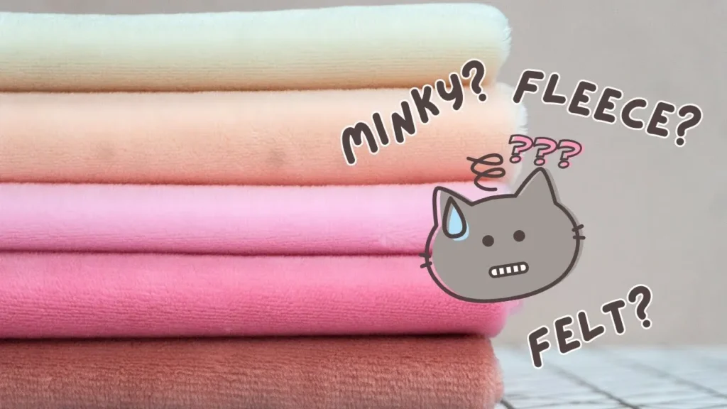 Stacked soft fabric pieces in various pastel colors with a cartoon cat confused about whether the fabric is minky, fleece, or felt.