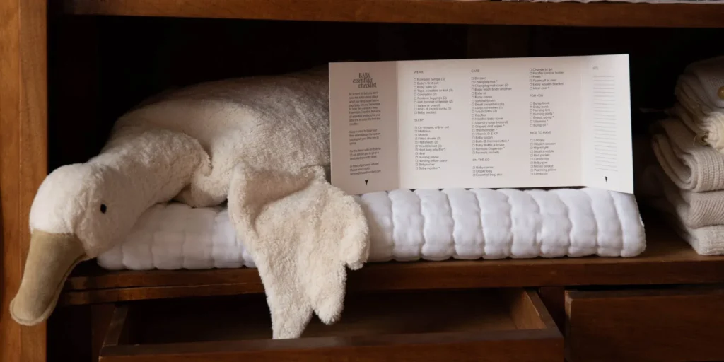 Soft plush duck and baby items on wooden shelf with checklist card.