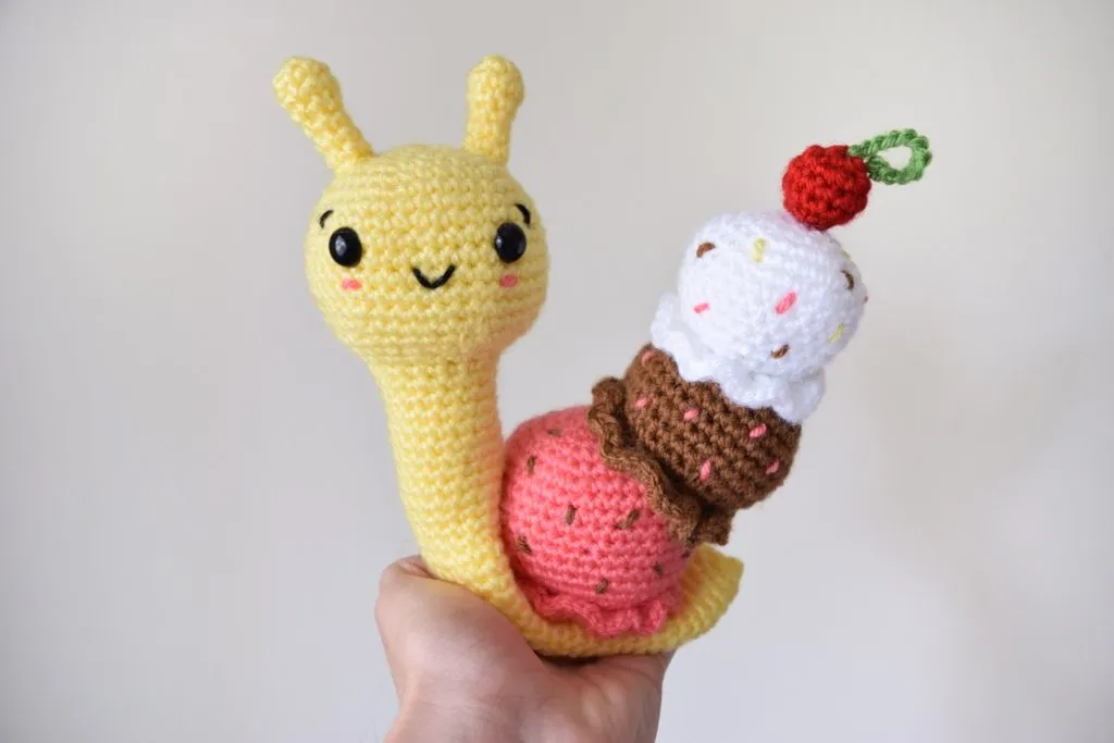 Hand holding a colorful crocheted snail with ice cream shells and black safety eyes