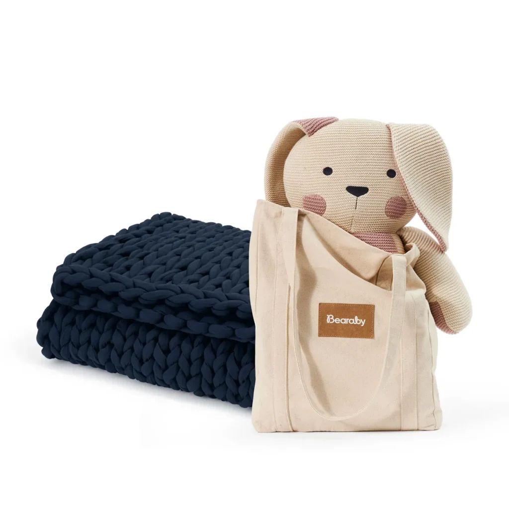 Knitted stuffed toy and navy chunky knit blanket in a beige tote bag