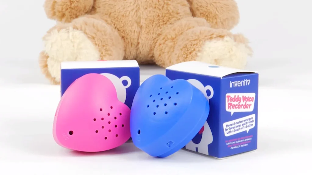 Pink and blue heart-shaped voice recorders with packaging in front of teddy bear.