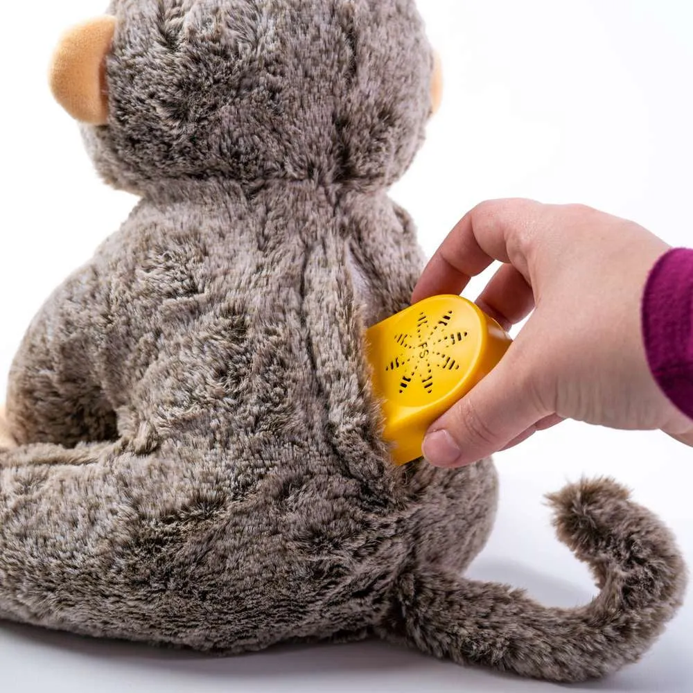 Hand placing yellow sound device into back of gray plush monkey toy.