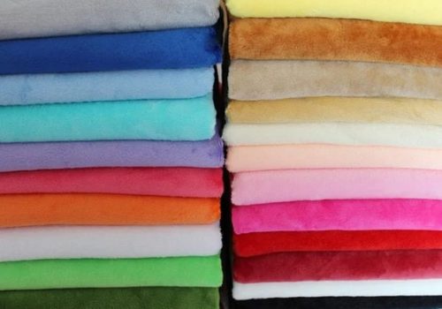 Plush Fabric Colors Neatly stacked colorful plush fabric sheets in various shades including blue, pink, green, and brown for sewing or crafting.