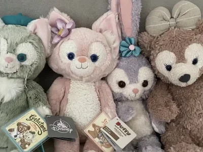 Four Disney plush toys sitting side by side on a couch with tags attached.